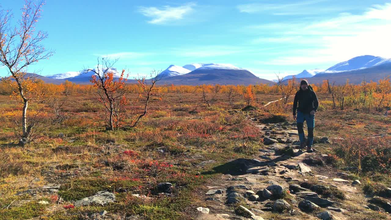 abisko 국립 공원의 하이커가 카메라를 향해 걸어 아름다운 경치 좋은 가을 알파인 풍경에서 멀리 눈으로  ⁇ 인 산과 함께