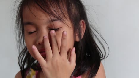 closeup shot of a cute asian toddler, with big round eyes, putting an artificial eyelash but failed and ends up laughing at herself