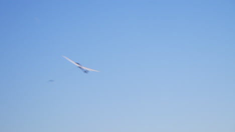 View-from-below-at-starting,-ascending-glider-on-a-wire-moving-from-right-to-left-under-blue-sky-