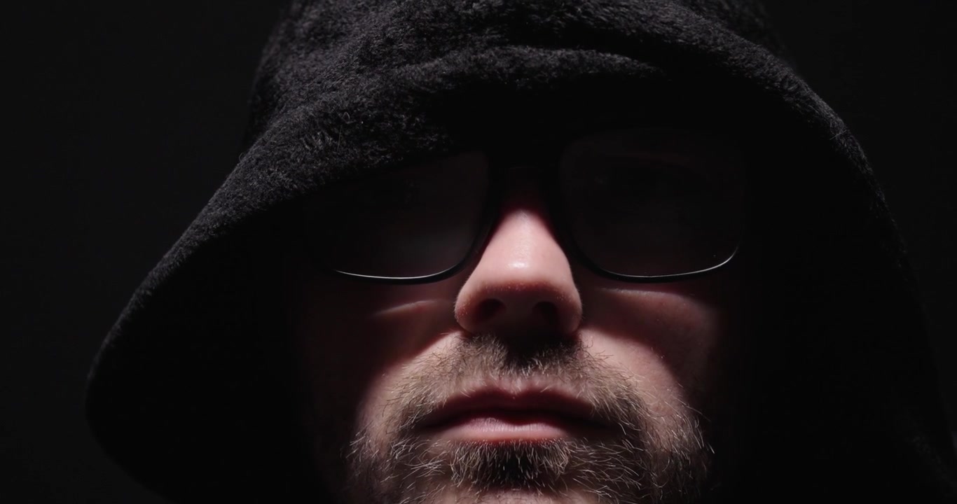 Close-up portrait of a hooded man in darkness, representing mystery, anonymity, secrecy, and cybercrime concepts.