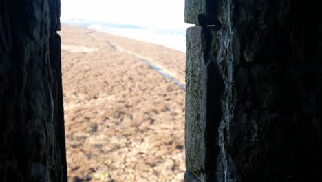 View-through-ancient-stone-castle-window-overlooking-moorland-highland-countryside-wilderness-dolly-left