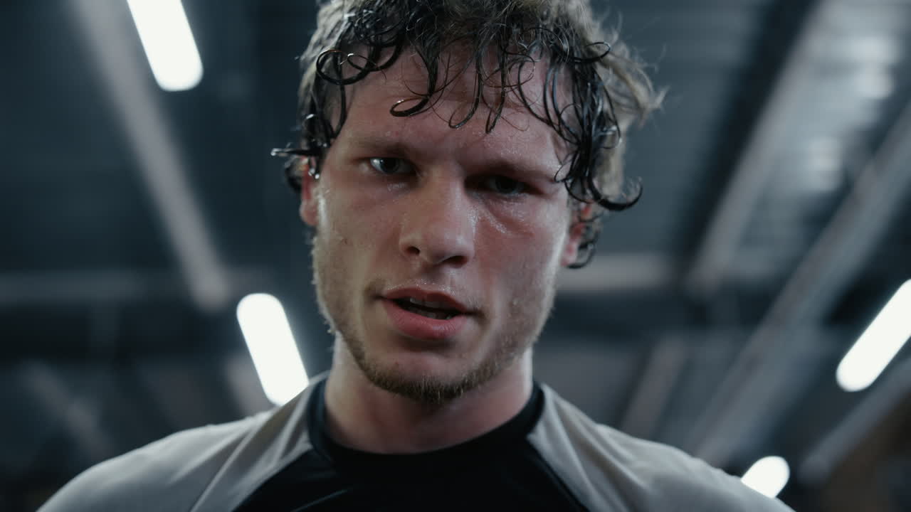 сонный кикбоксер смотрит на объектив в спортзале. спортсмен вытирает пот в спортивном клубе