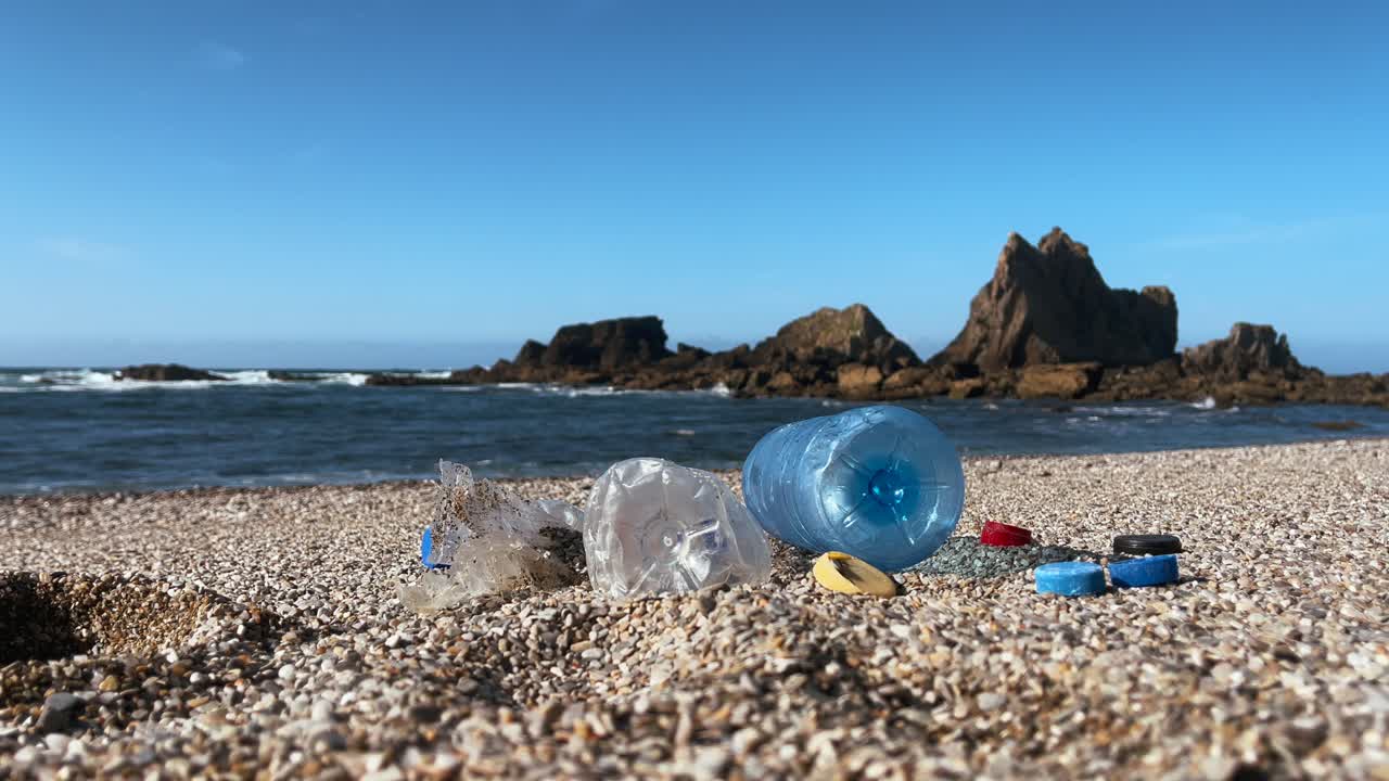 Plastic bottles and caps scattered on a pebbled beach near rocky ocean cliffs