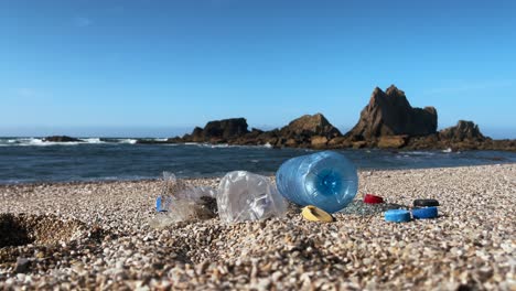 plastic bottles and caps scattered on a pebbled beach near rocky ocean cliffs