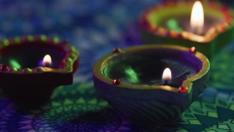 lit candles in decorative clay pots on patterned table top, focus on foreground, bokeh background