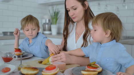 Zwei-Kleine-Brüder-Kochen-Mit-Ihrer-Mutter-In-Einem-Kleid-Zusammen-In-Einer-Weißen-Küche.-Burger-Lachen-Und-Lächeln.-Glücksfamilie-In-Der-Küche