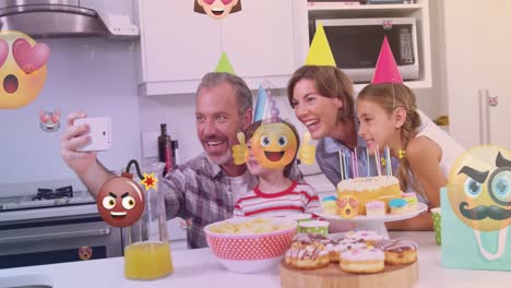 animación de emoticones sobre una feliz familia caucásica durante una fiesta de cumpleaños tomando selfies