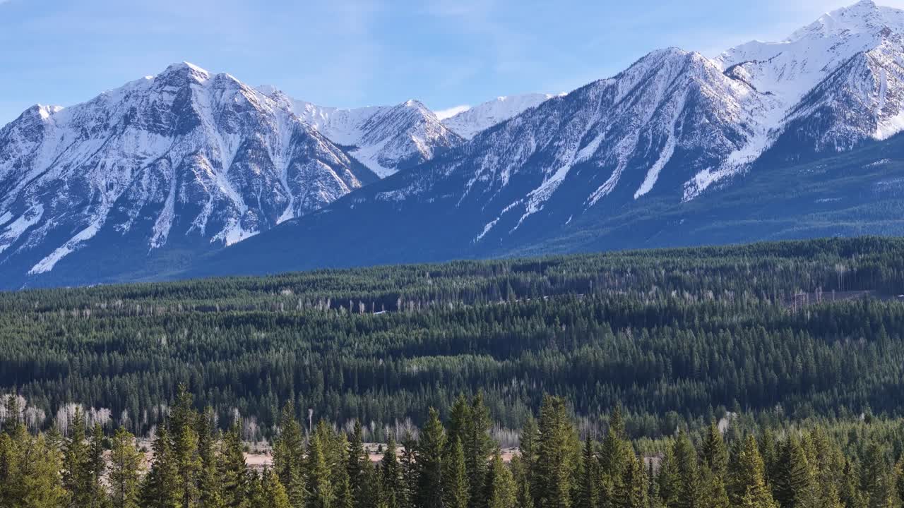Majestic Canadian Rockies with some snow covered peaks and evergreen and pine trees in the foreground