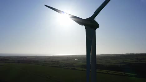 aerial of wind turbine on green field, truck left, sun flare in background