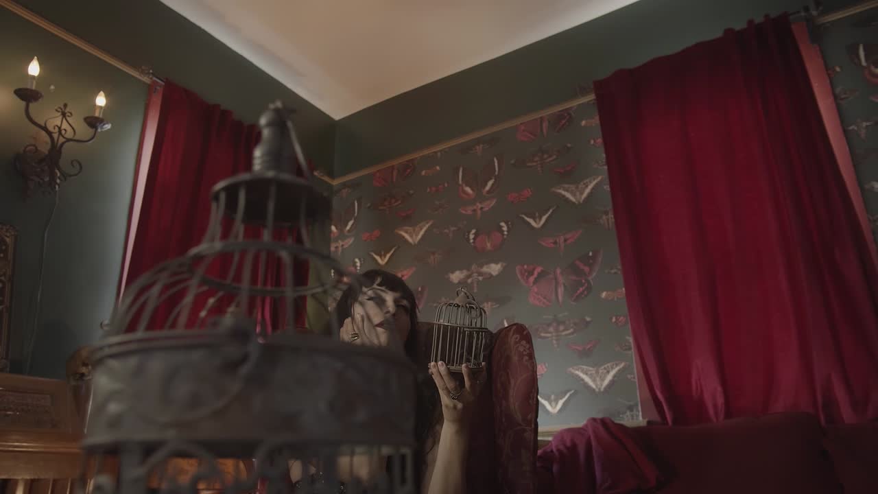 vista panorámica de una mujer romántica sosteniendo una jaula de metal con una cortina roja en el fondo