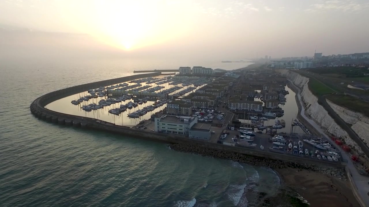 Bidikan drone yang naik perlahan dari marina di laut Inggris dengan matahari terbenam di latar belakang