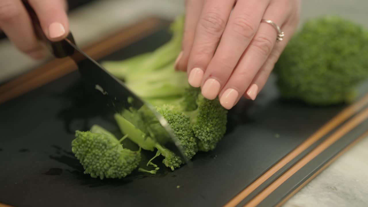 Stems of broccoli are slices through with a knife on a cutting board