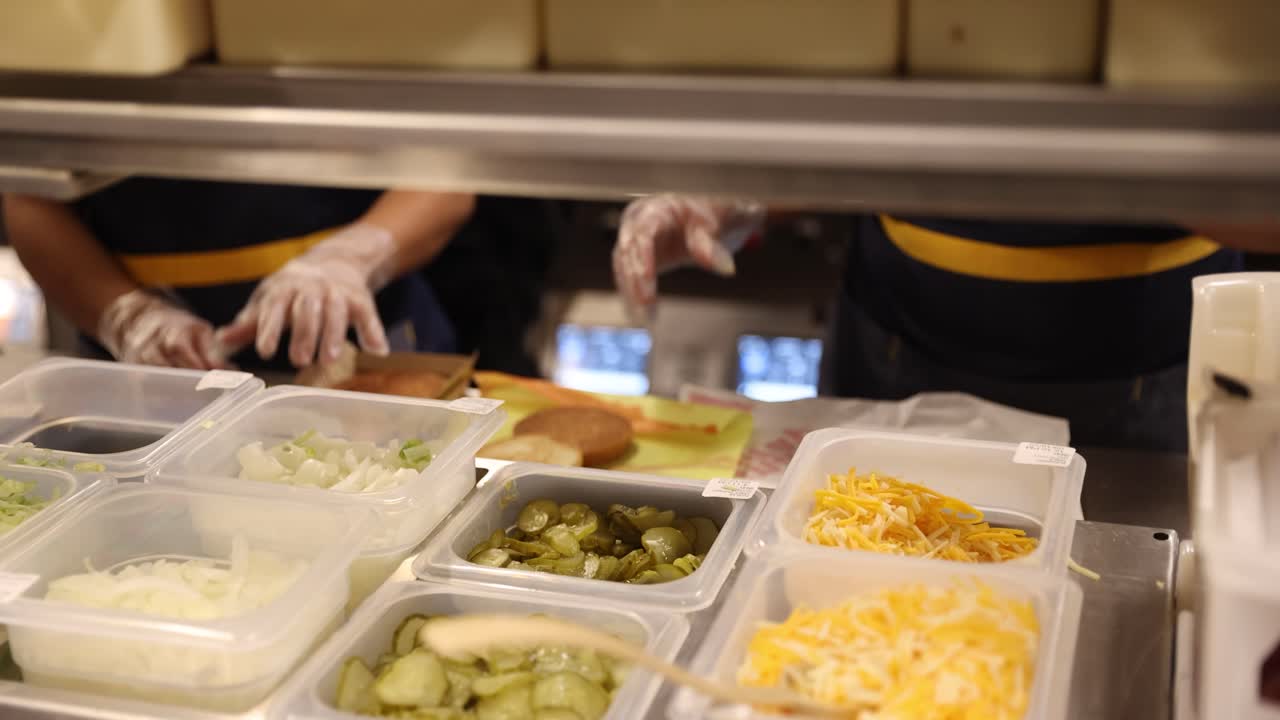 Close-up of hands assembling a fast food burger in a commercial kitchen. Generic food prep scene focused on motion and technique