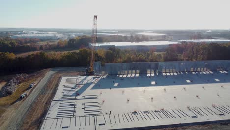 a medium drone shot orbiting a heavy duty crane while it lowers a concrete panel with braces attached