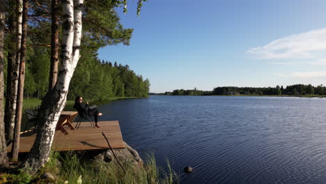 Woman-sitting-with-glass-of-wine-and-book-on-deck-by-sea,-vacation-in-Finland