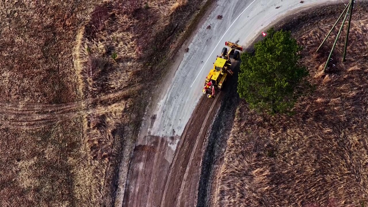 Veihøvel former grusvei og svinger på motorveien, luftfoto