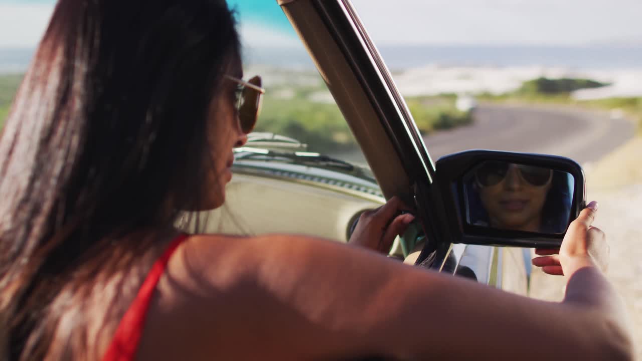Donna afroamericana che regola lo specchietto retrovisore laterale mentre è seduta in un'auto decappottabile