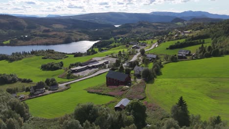 aerial view of a valley in norway, with lush green fields, a winding road, charming houses, and a serene lake surrounded by majestic mountains