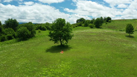 girl in orange dress relaxing in green fields of lika region, croatia