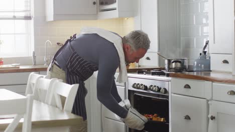 happy caucasian man wearing apron, standing in kitchen, cooking dinner