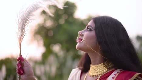 an indian newly wed woman plays with a white flowered grass in a field at sunset or sunrise