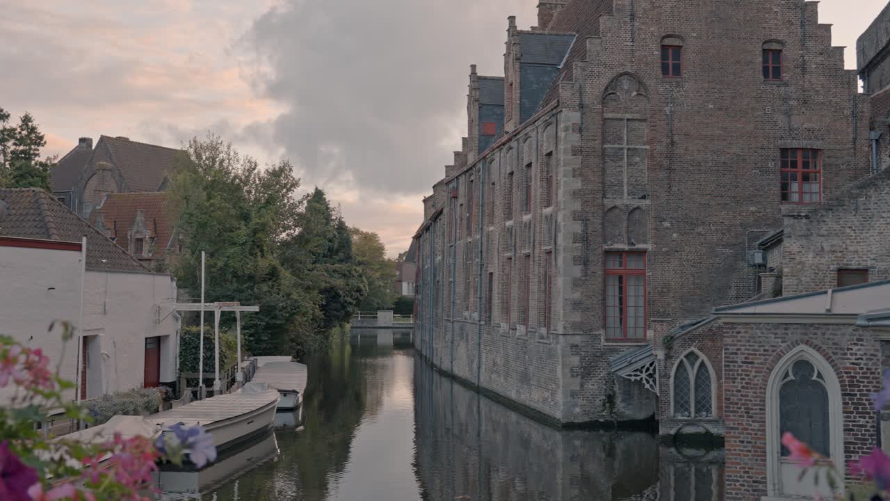 An atmospheric view at dusk in Bruges, Belgium, capturing a tranquil canal flanked by the imposing Gothic brick architecture of the Sint-Janshospitaal (Old St. John's Hospital)