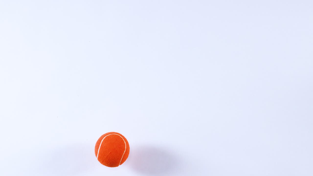 una pelota de tenis naranja rebotando en una superficie blanca
