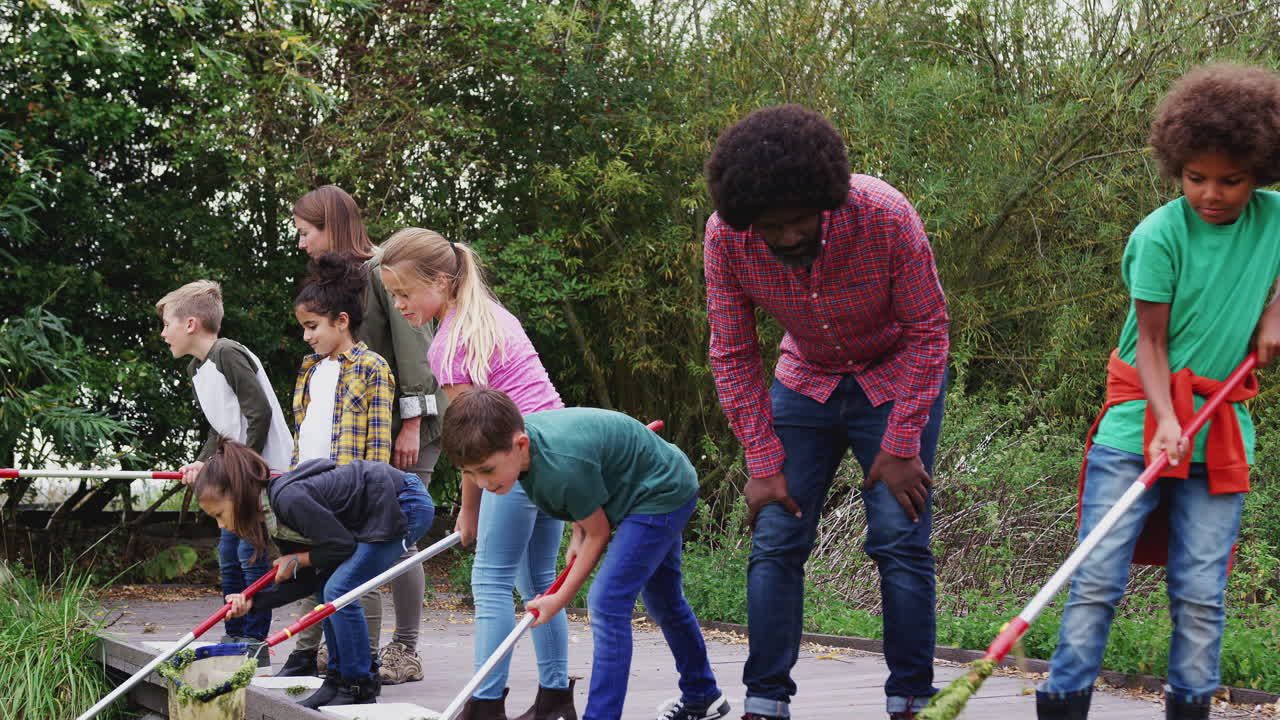 Volwassen groepsleiders laten een groep kinderen op een buitenactiviteitenkamp zien hoe ze waterdieren kunnen vangen en bestuderen.