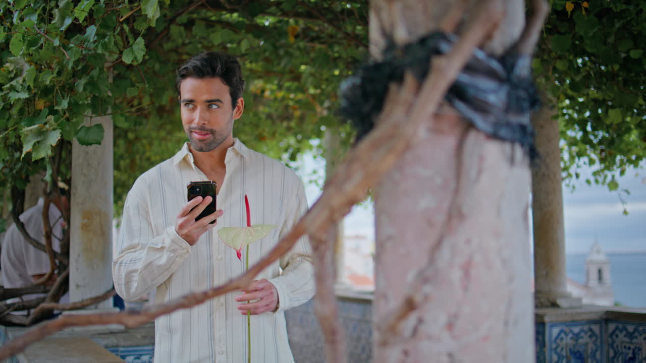 Smiling man looking cellphone holding flower at date closeup. Brunette waiting