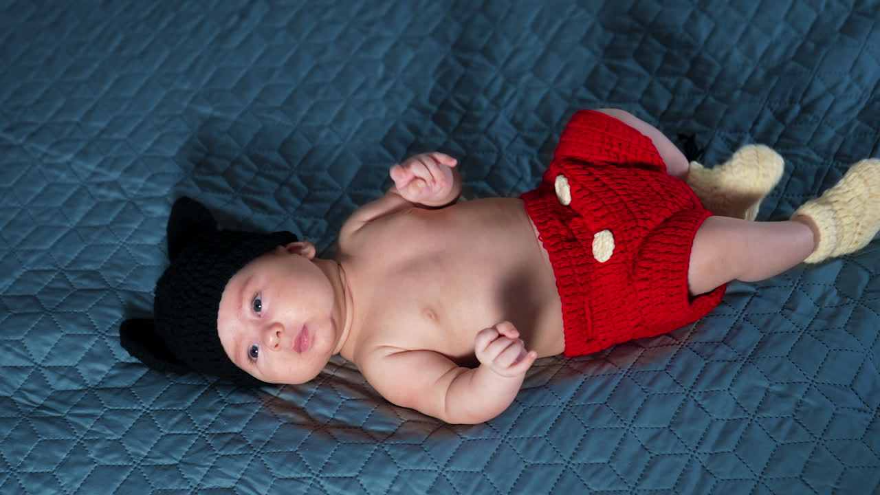 Caucasian little kid wearing costume of Mickey Mouse on bed. Adorable kid in funny costume at the grey backdrop. Top view.