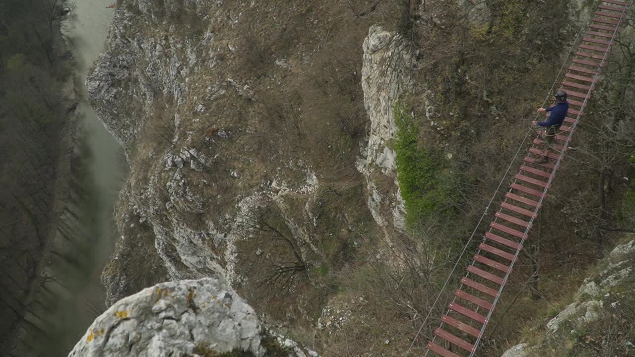 alpinista con arnés de seguridad y engranajes parado en medio del puente colgante en vía ferrata - casa zmeului en rumania
