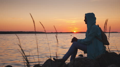 woman sits on a rock near a picturesque lake at sunset