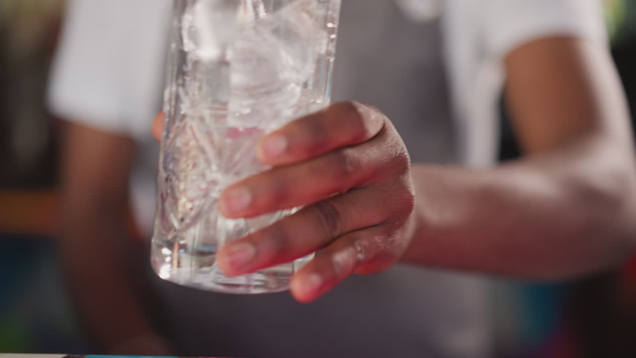 바맨은 스쿠프 클로즈업으로 크리스탈 유리잔에 얼음을 부어줍니다. 아프리카계 미국인 바텐더는 술집에서 손님을 위해 테일을 준비합니다. 신선한 음료를 위한 아이스 큐브