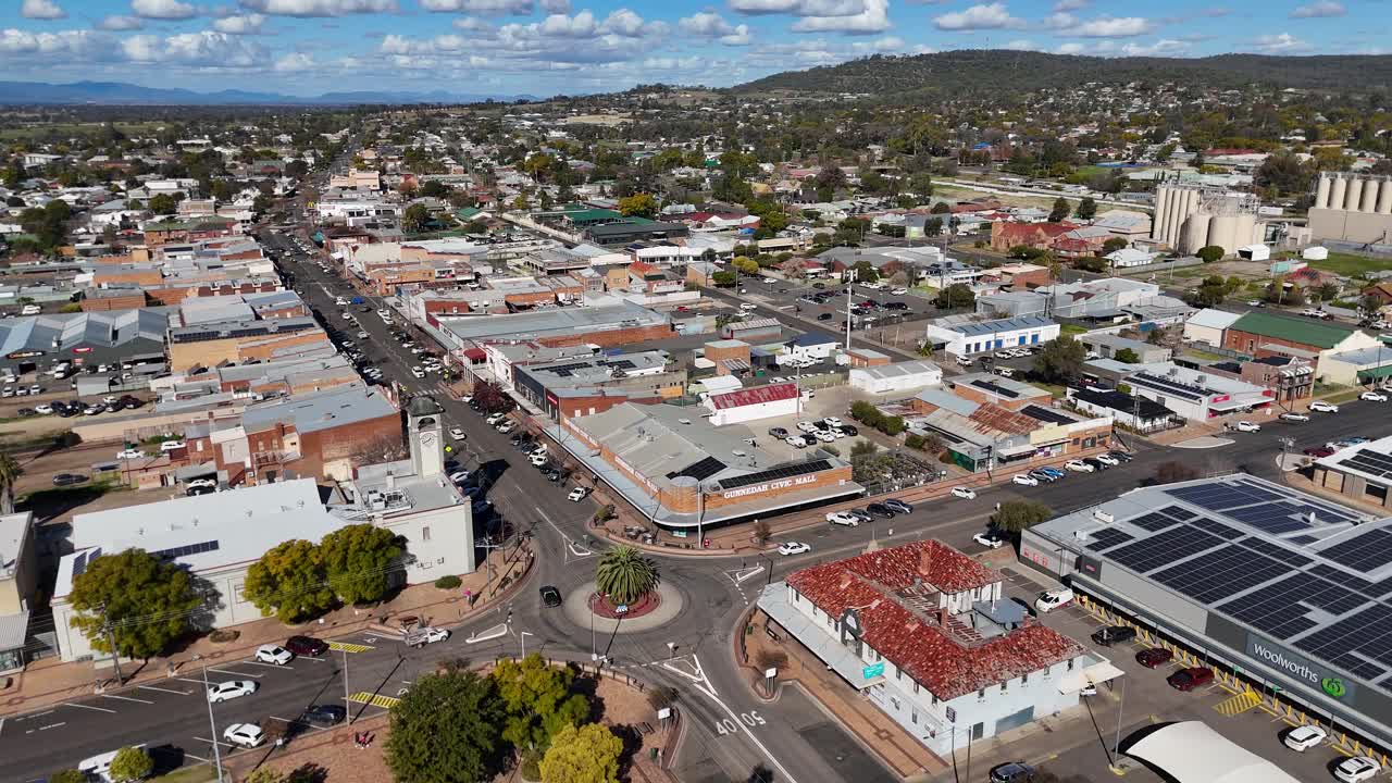 Drone footage glides above Glen Innes, NSW, revealing busy streets, parked cars, and commercial buildings under bright daylight with clear skies