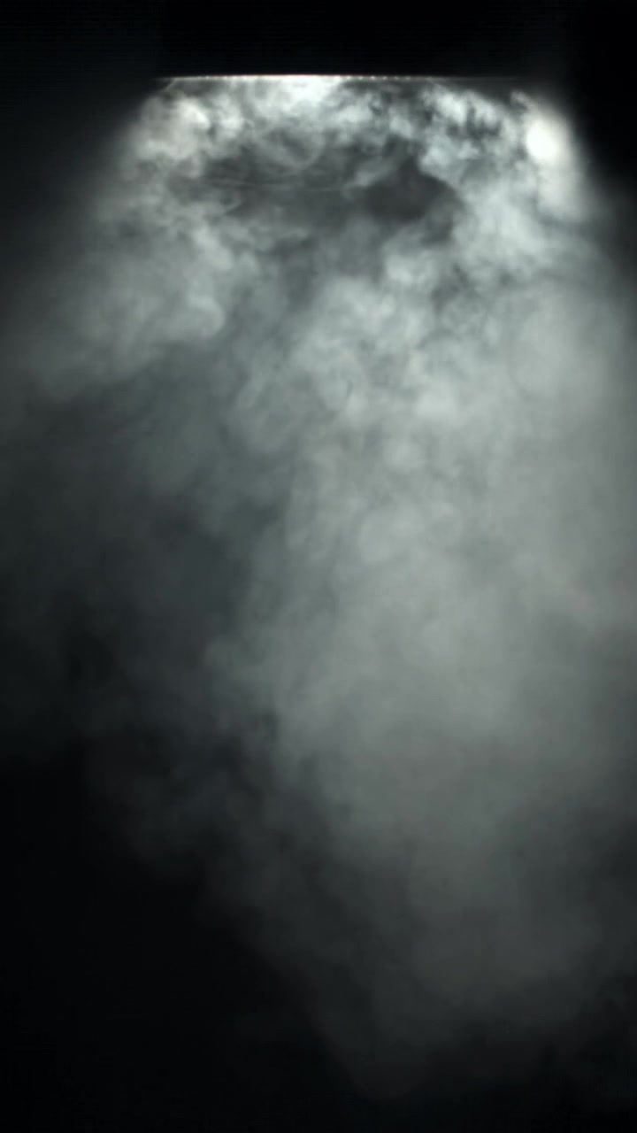 Fumo bianco denso che si muove in un fascio di luce su sfondo nero