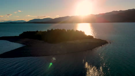 Malerische-Sonnenaufgangsansicht-Einer-Kleinen-Bewaldeten-Insel-Im-Lake-Pukaki,-Neuseeland-Mit-Sonnenbeschienenem-Hintergrund