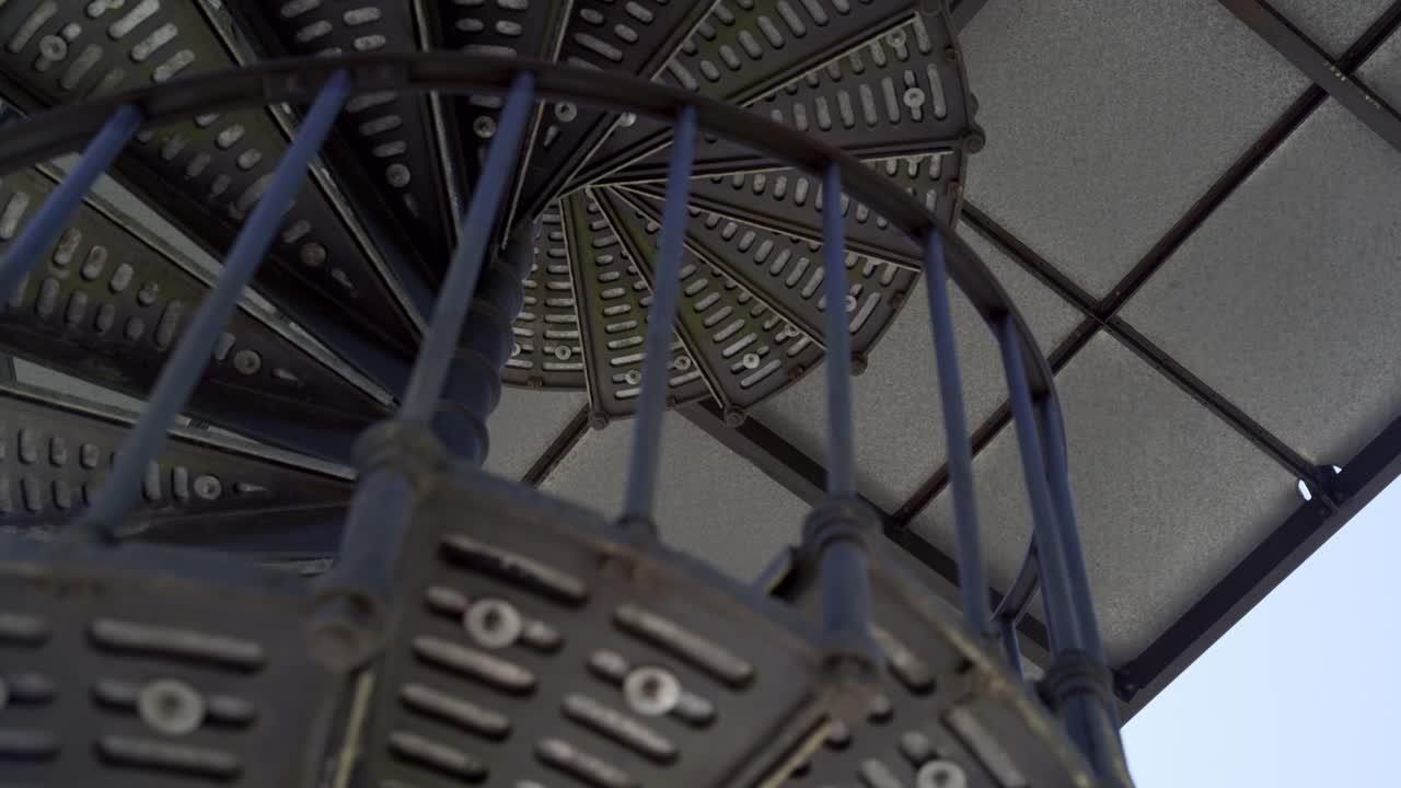 Solid steel spiral staircase in the shade, filmed from bottom to top with focus pull on the upper steps, close-up, 4K UHD, 25p