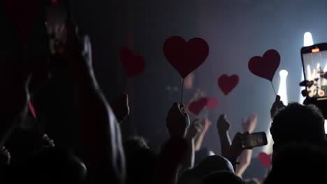 audience holding heart-shaped signs during a live concert performance with dramatic lighting effects