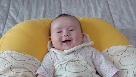 infant baby in great spirit laughing out loud lying on the yellow cushion on the bed, close-up portrait shot