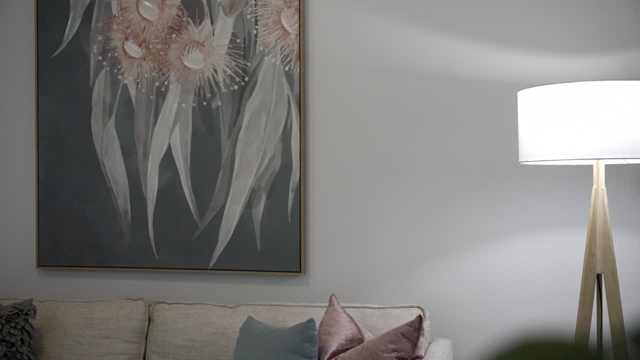 Pan from behind plant showing lounge room with lounge, pillows, paintings, lamp, coffee and table