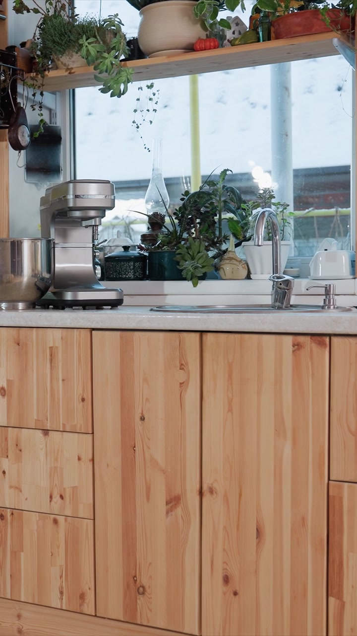 Giovane donna che prepara il cibo in una cucina moderna. La donna maneggia una ciotola per mescolare e aziona un robot da cucina. La scena include una tovaglia bianca e una finestra con vista esterna innevata