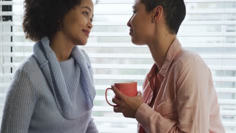 Lesbian-couple-having-coffee-sitting-on-window-sill