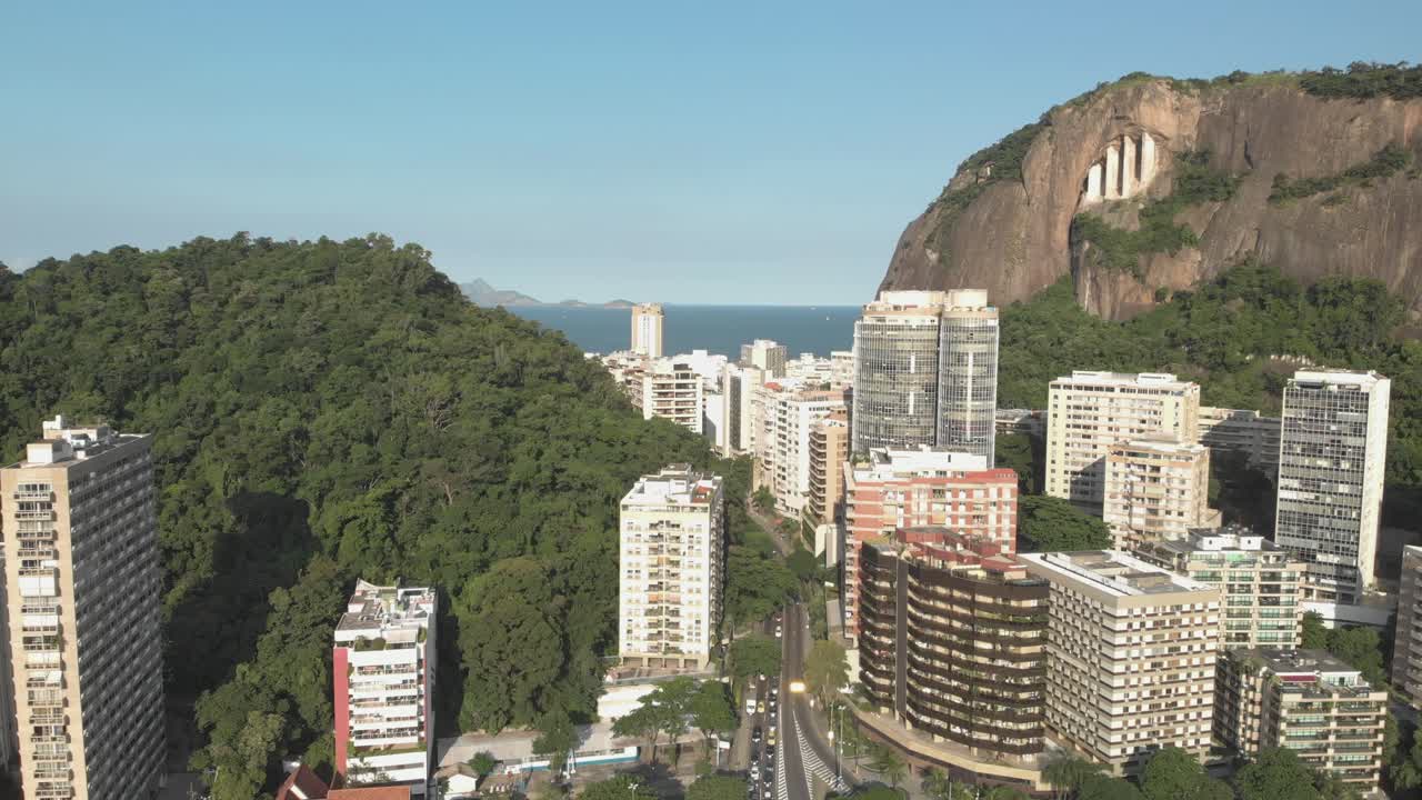 Movimento aéreo lento recuando com vista para edifícios residenciais altos, com uma montanha ao fundo, revelando um cruzamento de rodovias com tráfego abaixo