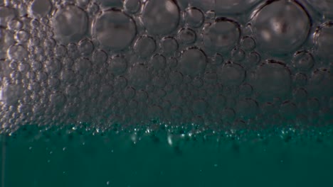 thick layer of clear bubbles gathering on top of aqua colored liquid, macro