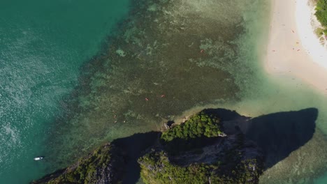 scenic side view of two limestone islets near ao nang, krabi, covered in tropical greenery and surrounded by emerald sea, with boats anchored near the cliffs and reef.