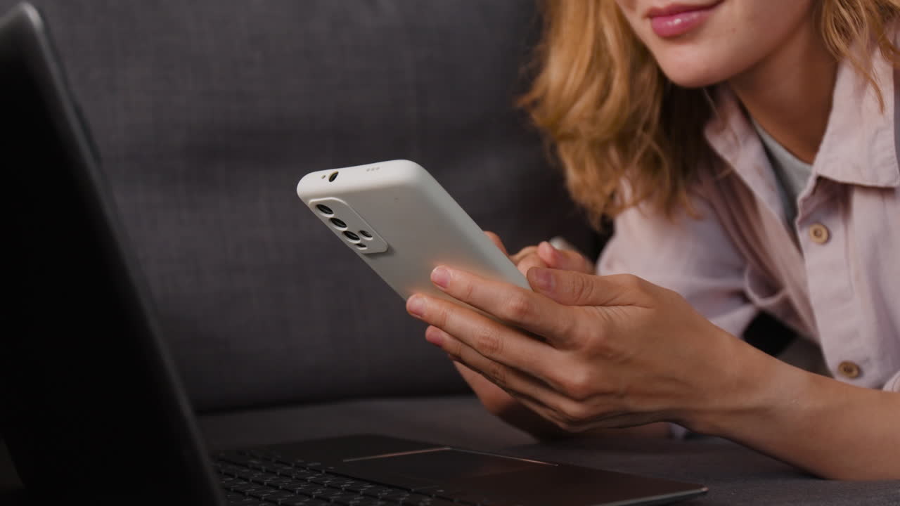 Woman using a smartphone and laptop on a sofa
