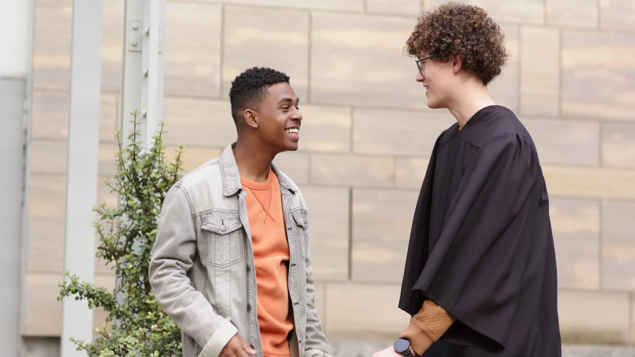 Diverse male friends offering cap holding diploma showing phone in wallet-style case in courtyard