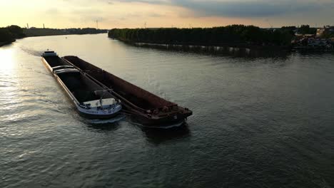 buque de carga con barcazas conectadas a un lado moviéndose lentamente en un río tranquilo