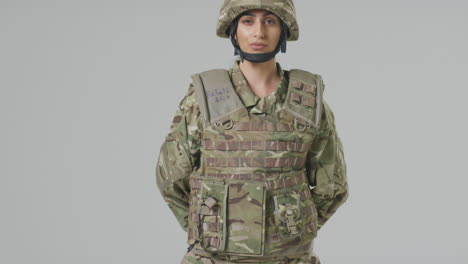 full length studio portrait of serious young female soldier in military uniform on plain background