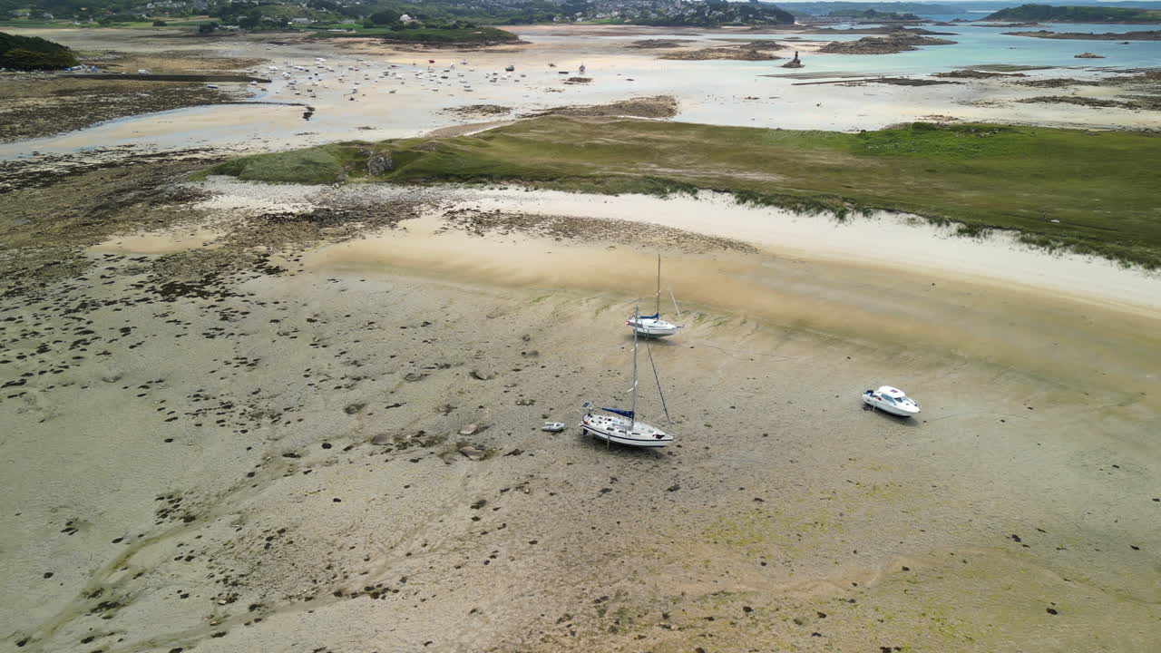 Riprese aeree ad arco di tre piccole barche adagiate su una spiaggia sabbiosa con la bassa marea